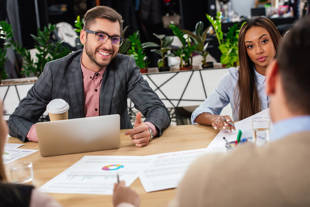 two men and a woman sitting a work table with laptop and paper discussing business liability and commercial insurance
